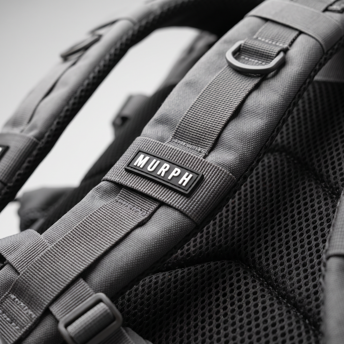 Gros plan de la bretelle et du logo brodé du sac Murph Hero 25L gris