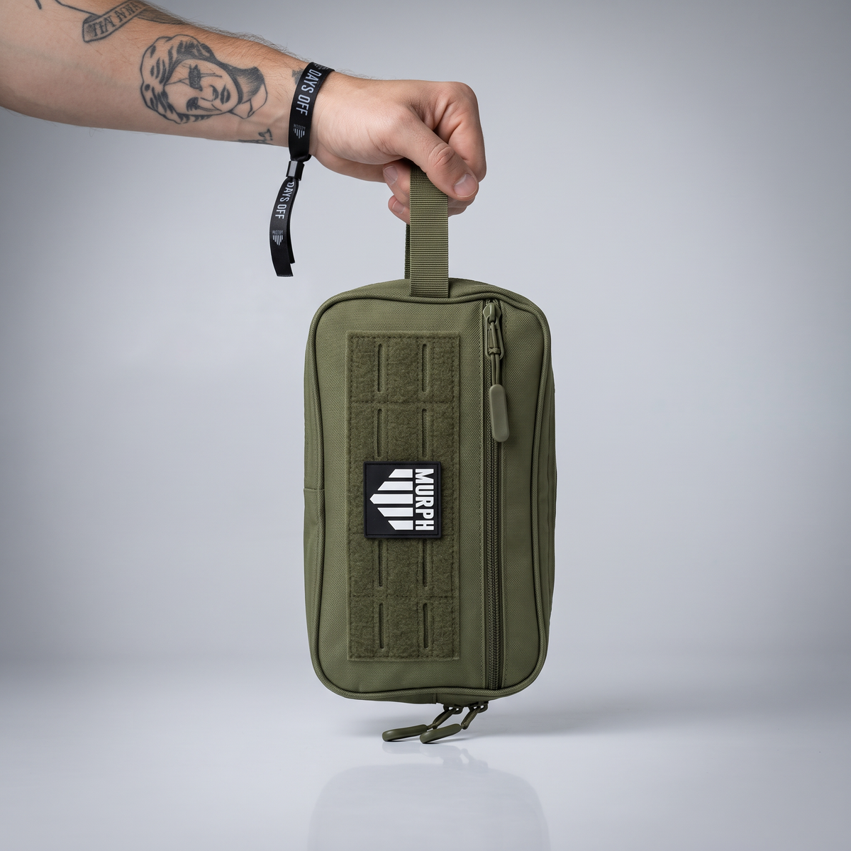 Trousse de toilette tactique Murph kaki portee a la main par la sangle laterale