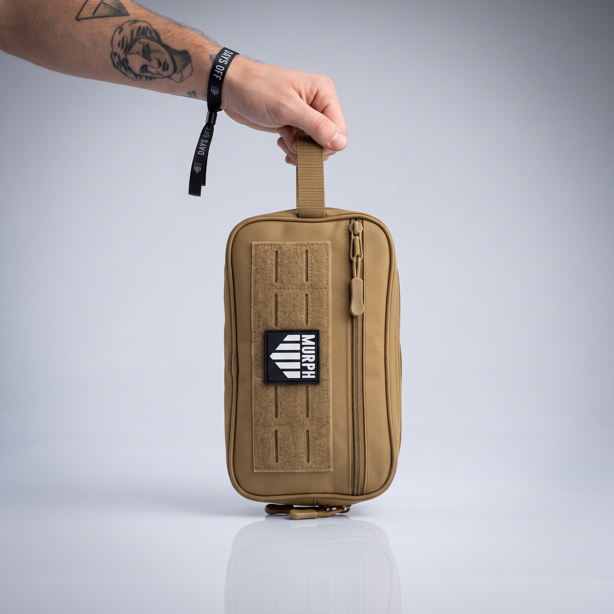 Trousse de toilette tactique Murph marron portee a la main par la sangle laterale
